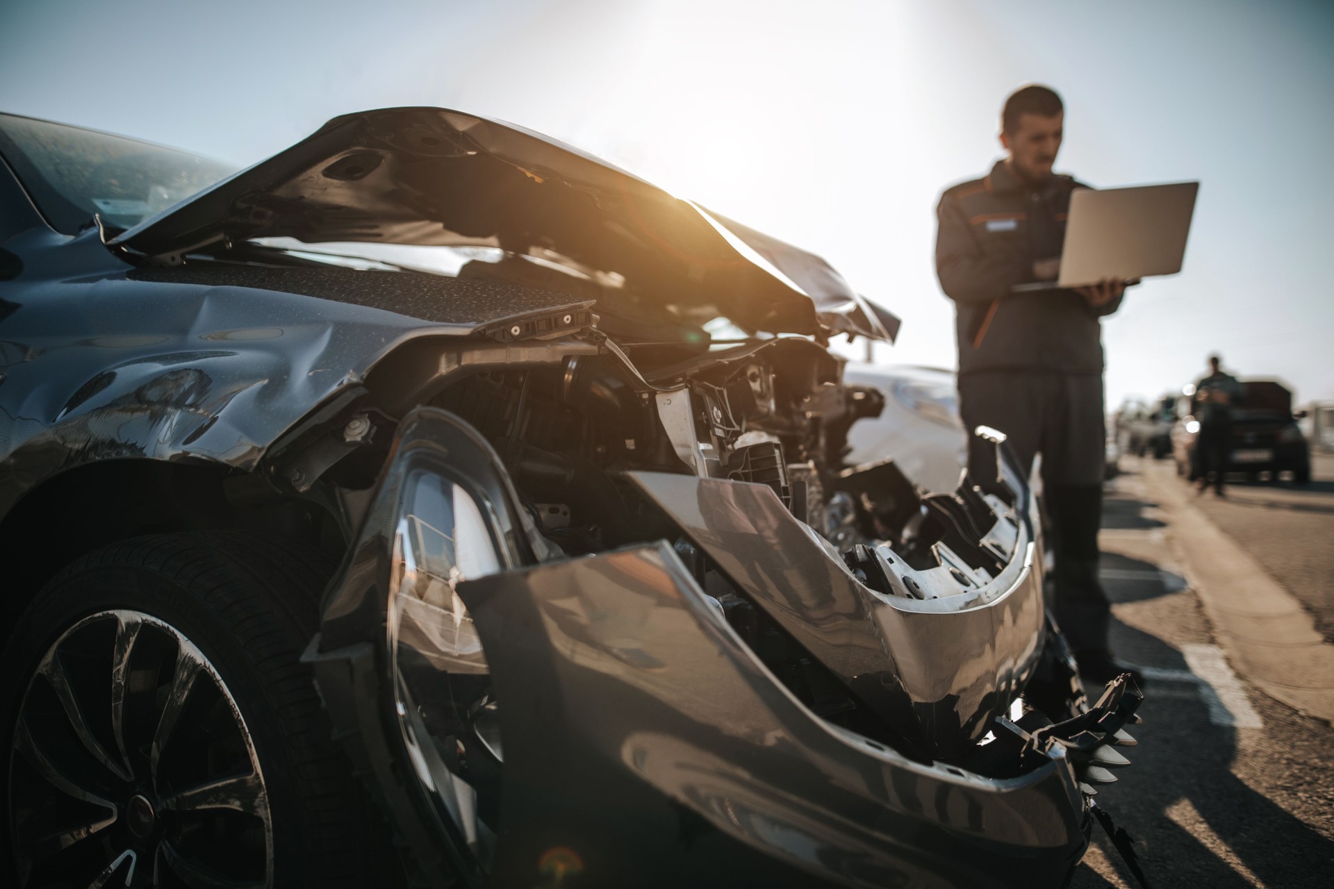 Mechanic working on laptop in front of damaged car on parking lot