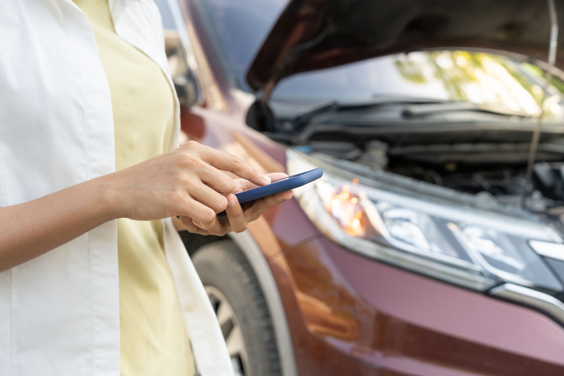 breakdown, broken car, repair. Woman uses mobile phone check insurance premiums through application due to car accident . Find garage to get car fixed during country tour, waiting for help, emergency.