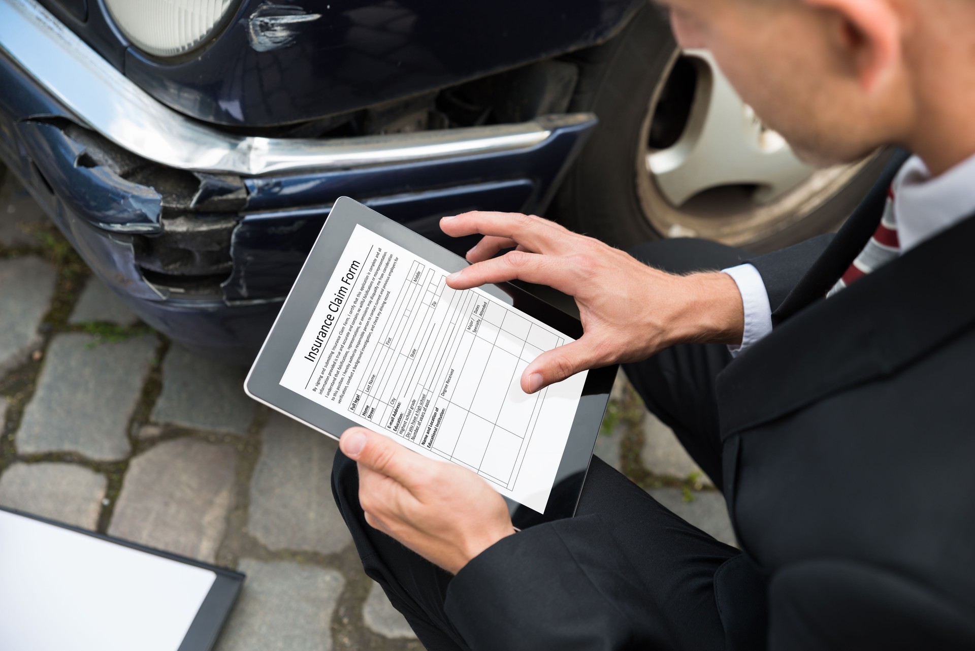 Man Holding Digital Tablet Examining Damaged Car