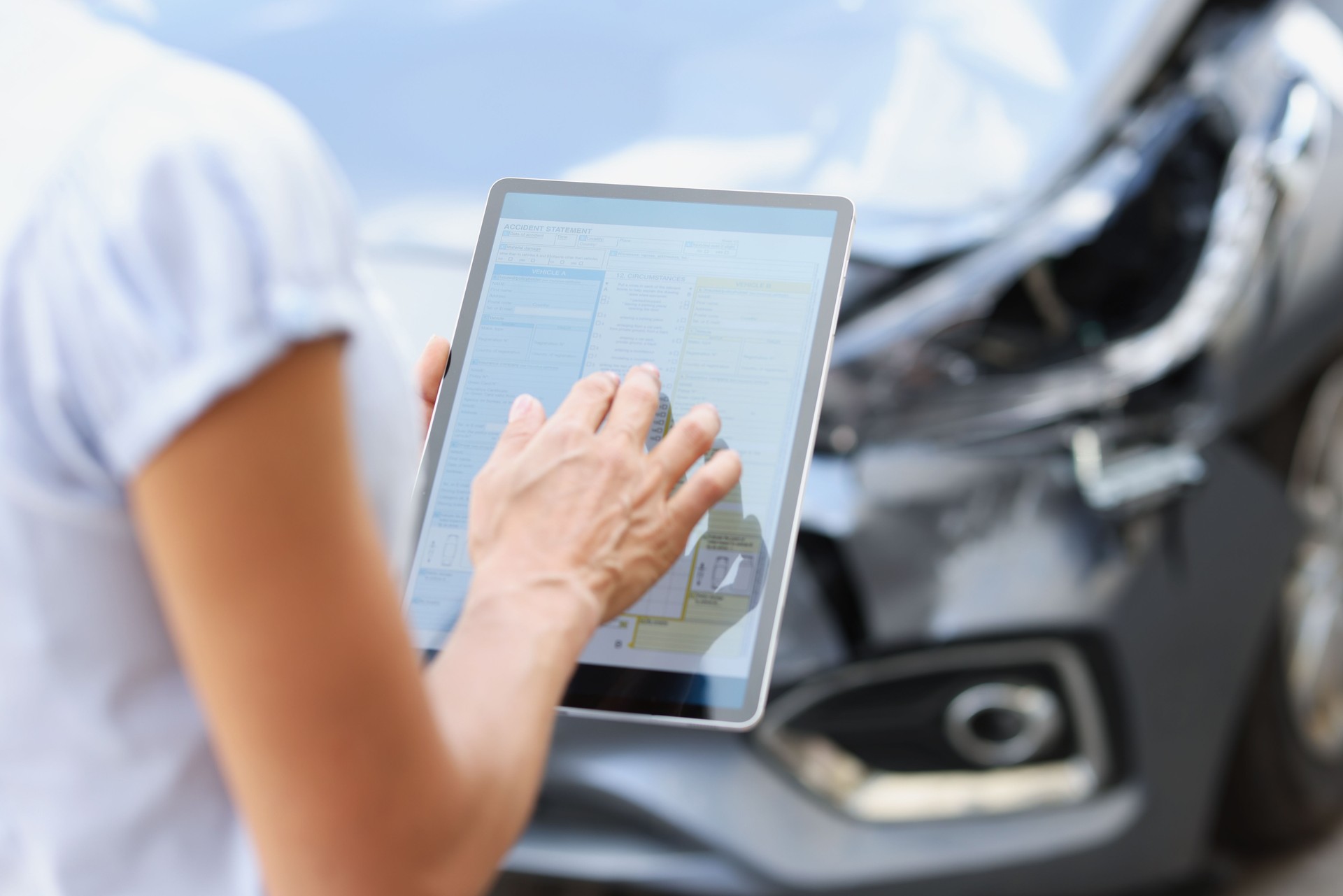 agent driver filling out insurance claim on digital tablet against background of broken car closeup